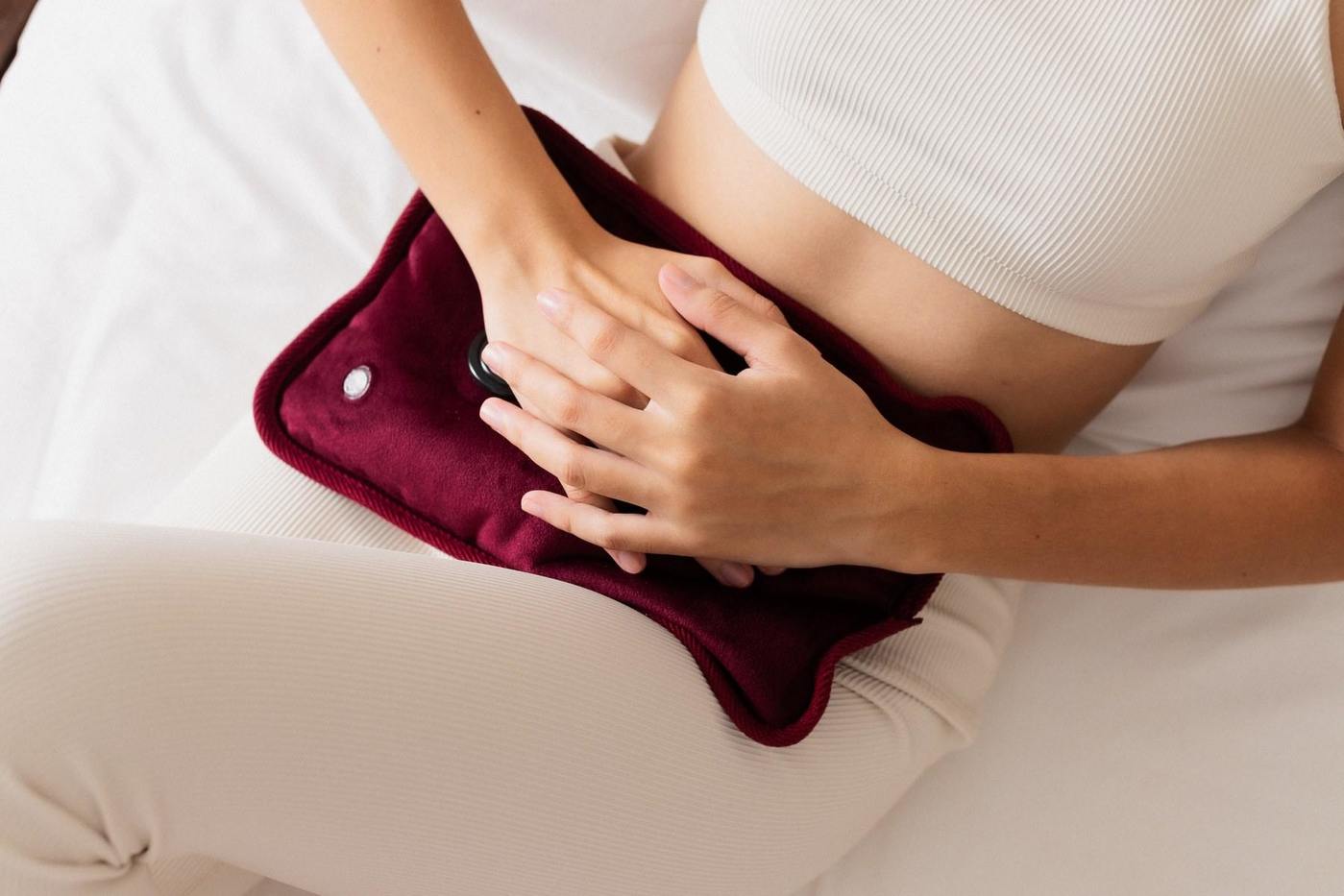 ベッドに座り、お腹に湯たんぽを当てて手を添えている女性