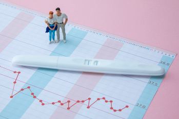 基礎体温表の上に置かれた妊娠検査薬と、寄り添うカップルのミニチュア人形